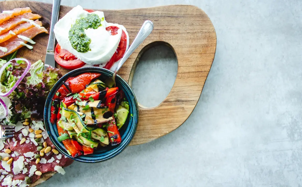 Assiette de légumes grillés, mozzarella, tomates et saumon sur une planche en bois